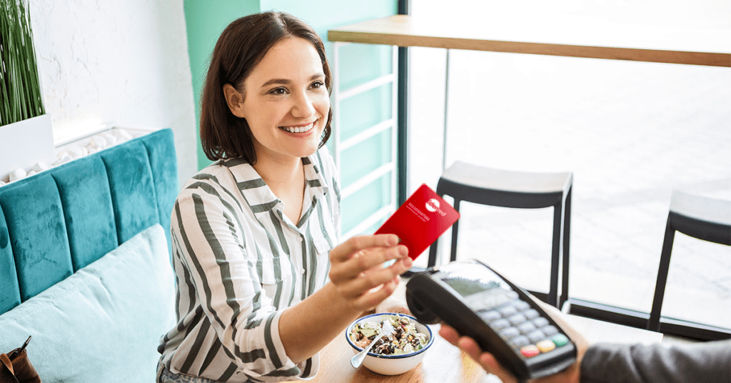 femme en train de tendre sa carte edenred cheques repas pour payer l'addition dans un bar