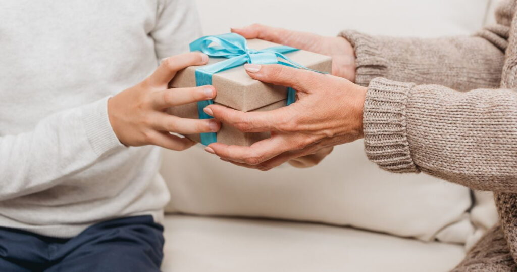 personne assise sur un fauteuil qui donne un cadeau avec un ruban bleu à une autre personne